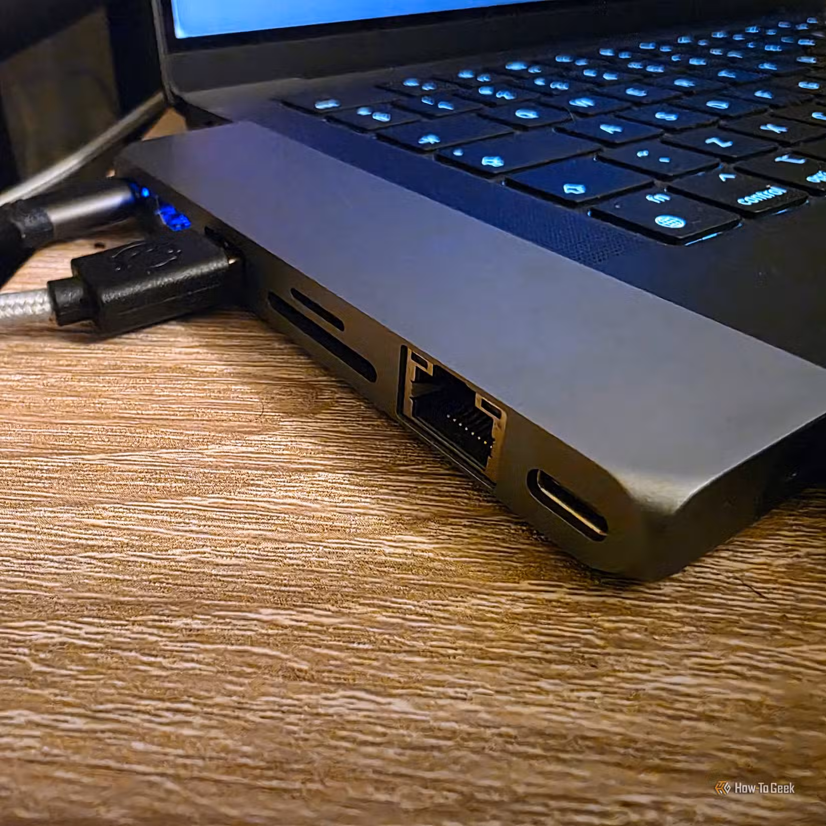 Close-up of a USB-C hub connected to a laptop, showing an Ethernet port, SD and microSD card slots, and a USB-C passthrough port for wired networking and expandable connectivity.