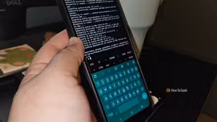 A hand holding a phone showing Termux downloading and installing packages.