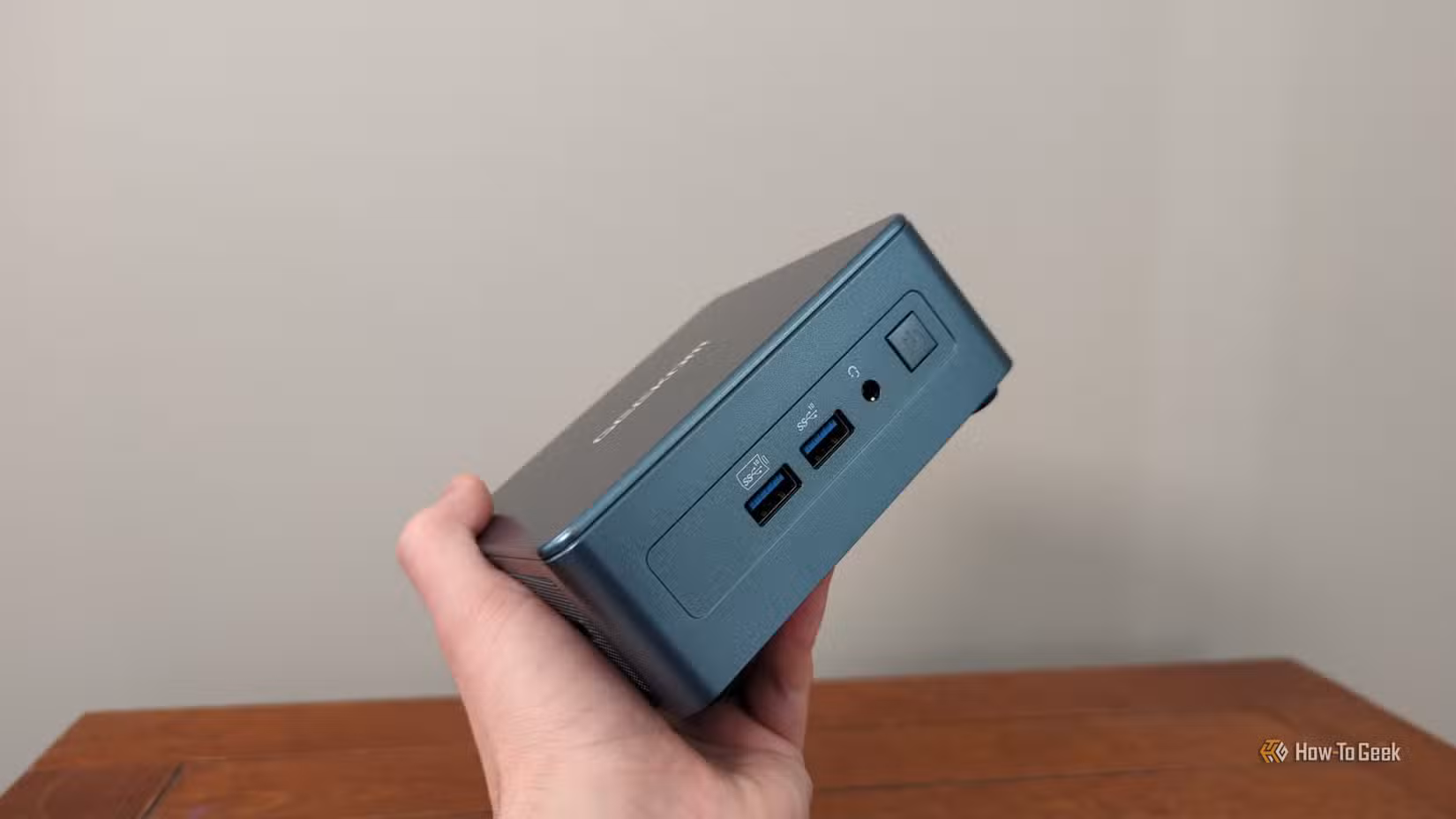 A person's hand holding a Geekom mini PC.