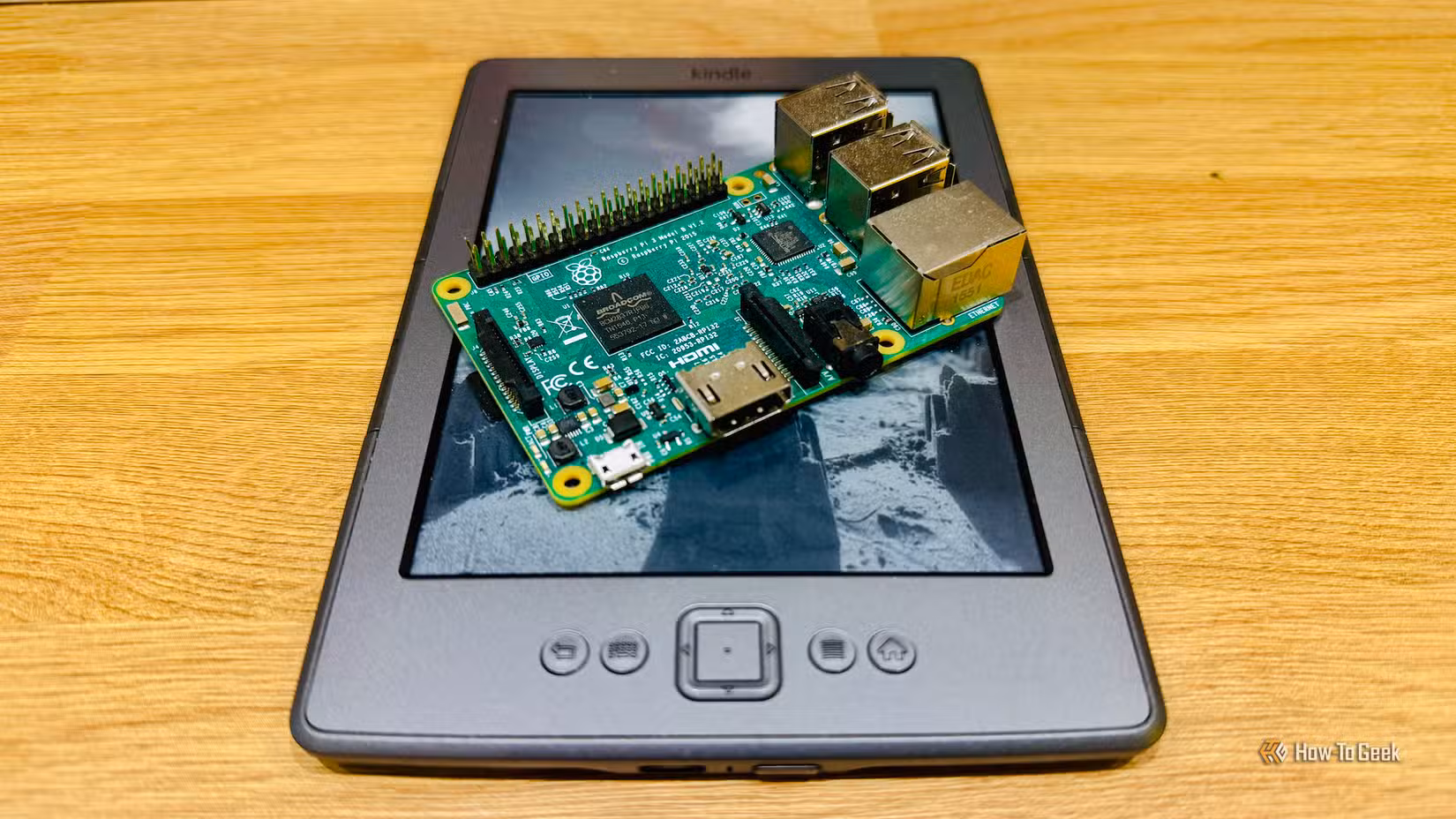 A Raspberry Pi 3B+ lying on top of a Kindle 4 on a desk.