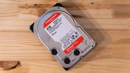 A Western Digital WD Red Plus 4TB NAS HDD sitting flat on a wooden desk.