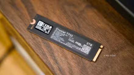 The back of the Crucial T710 NVMe SSD sitting on a walnut shelf.