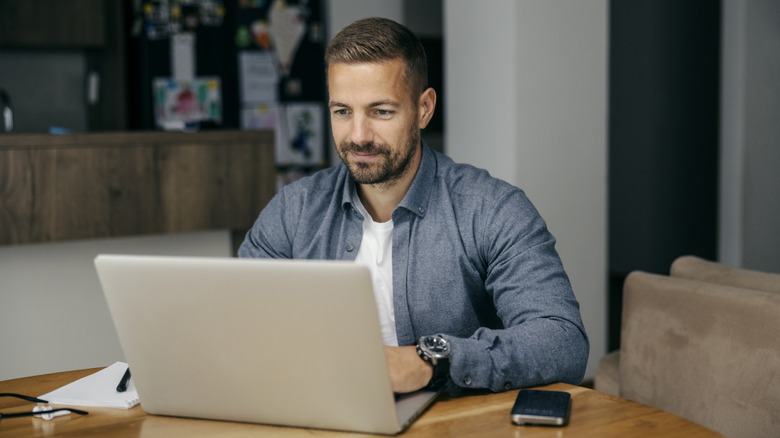 A man sitting behind a laptop smiling at a table.