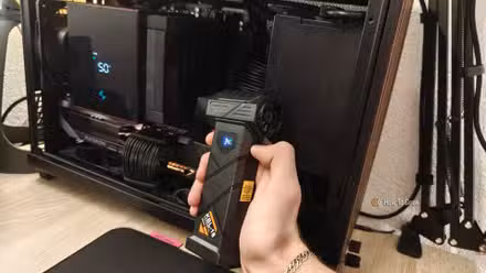 A hand holding an electric air duster in front of a gaming PC.