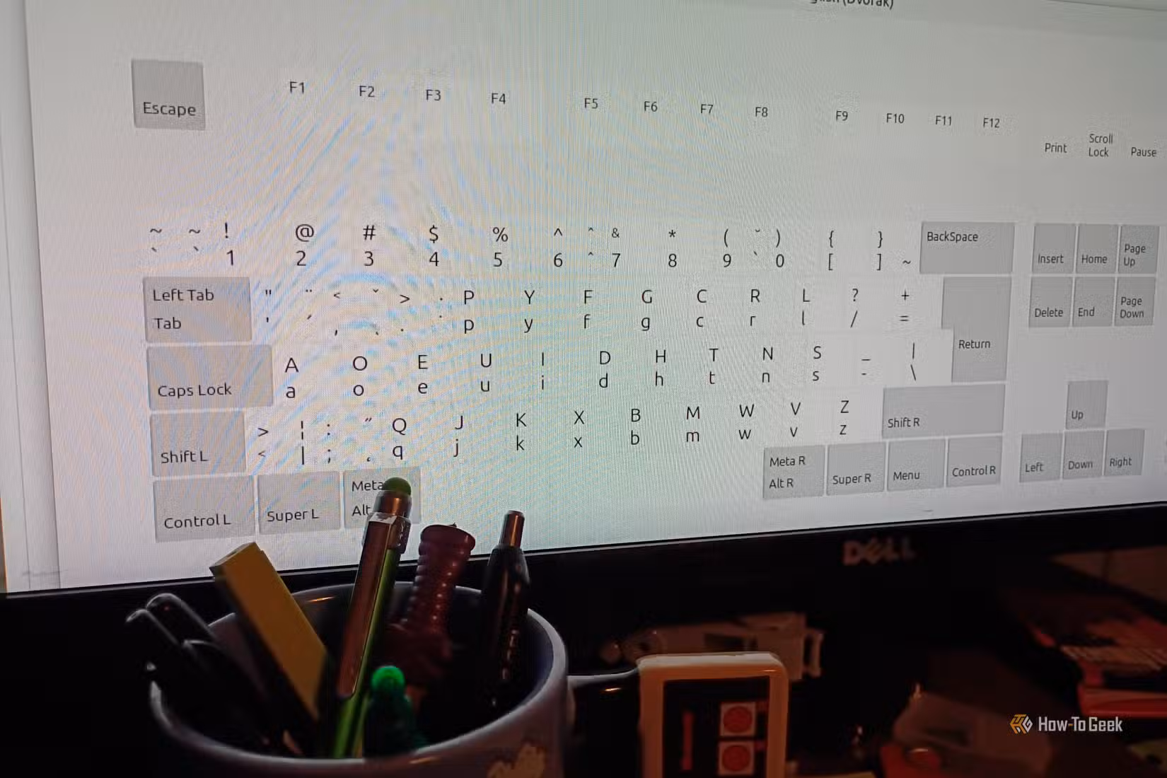 The dvorak layout on a computer monitor with a cup full of pens in front of it.