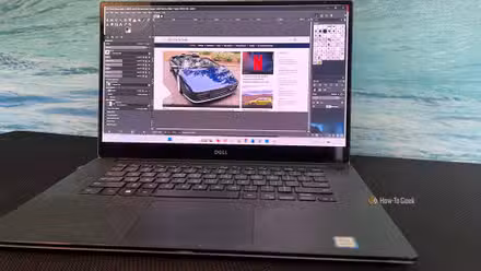 A laptop with GIMP editing an image of the HowToGeek.com homepage.