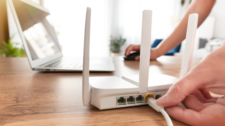 Hand plugging a cable into a router with multiple LAN ports and a WAN port.