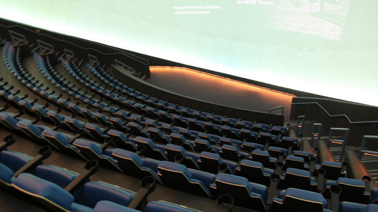 A massive theater screen is shown from above with stadium seating below.