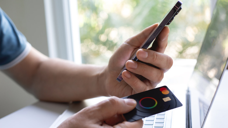A person holding a smartphone and a credit card.