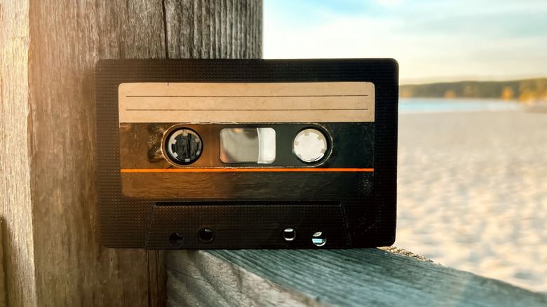 A cassette tape on a wooden ledge by the water.