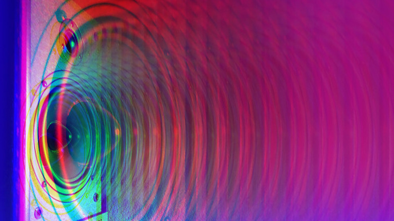 Close-up of a speaker cone with colorful sound wave ripples spreading across the image.