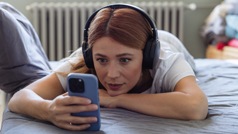 A woman wearing headphones and looking intently at her phone.