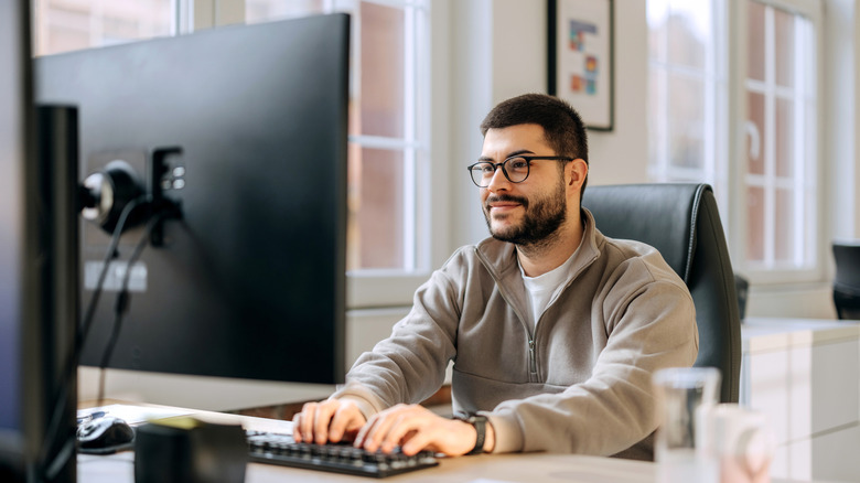 A man smiling while working at a desk with a computer.