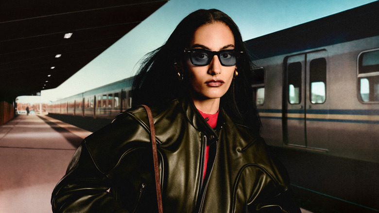 A woman wearing a pair of Ray-Ban Meta Audio smart glasses in front of a train.