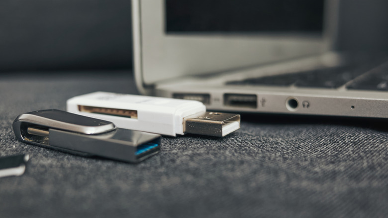 Two USB flash drives sitting next to each other, with an open laptop in the background.