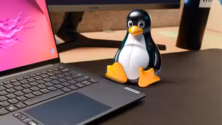 Linux mascot on a desk next to a laptop.