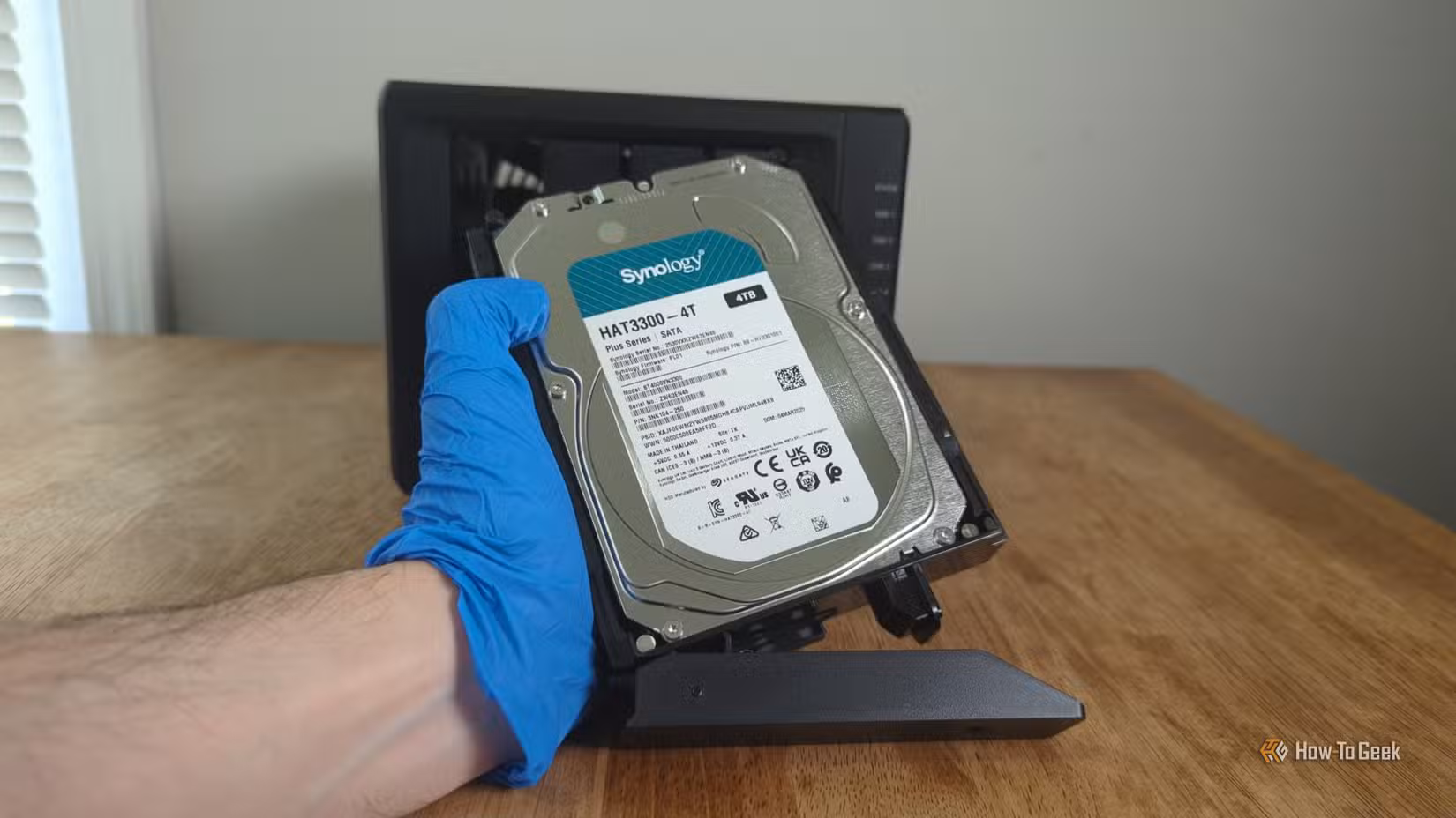 Person's gloved hand holding a Synology HDD in front the Synology DS425+ NAS.-2
