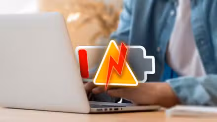 Person using a laptop with a low battery icon and an alert.