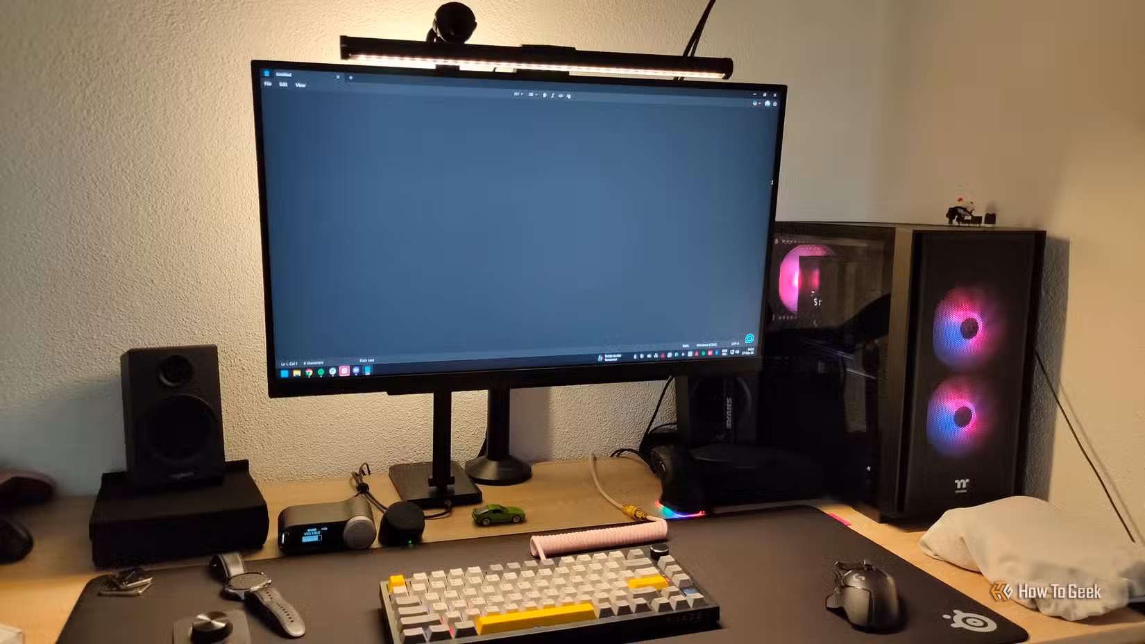 A desktop gaming PC desk with a monitor light, mechanical keyboard, wireless mouse, and numerous other gadgets.