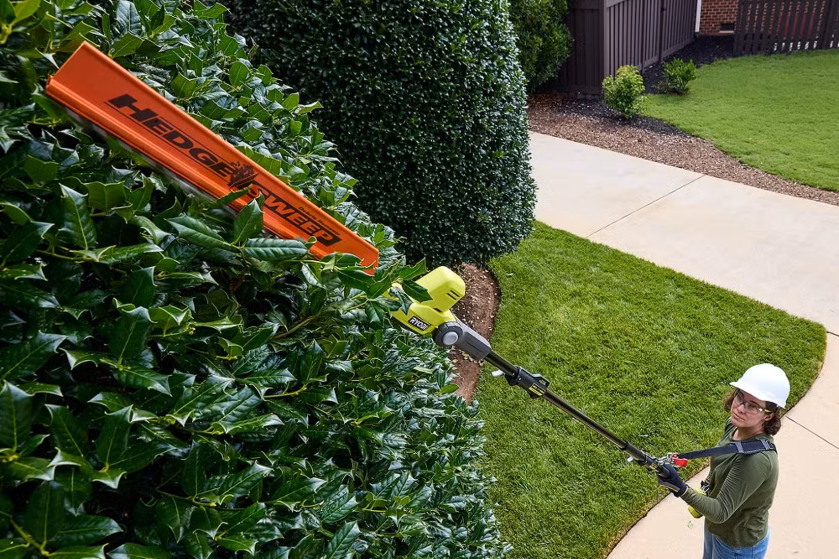 RYOBI pole hedge trimmer trimming a large bush.