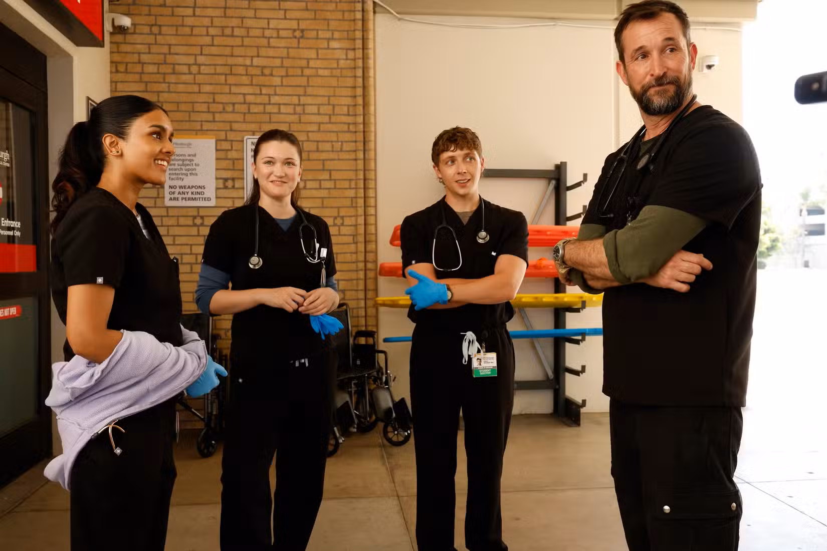 Shabana Azeez, Isa Briones, Gerran Howell, and Noah Wyle standing outside the ED, in scrubs and gloves, in The Pitt S2.