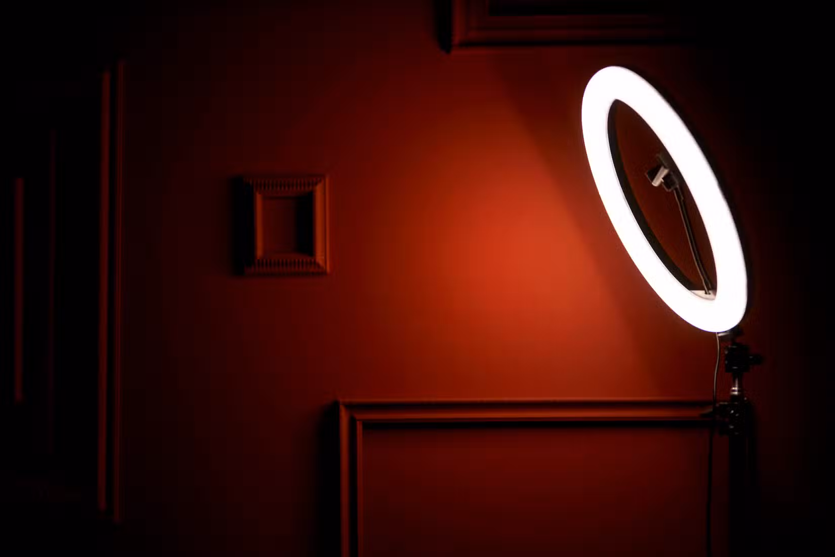 A ring light in a dim room lights up a nearby wall.