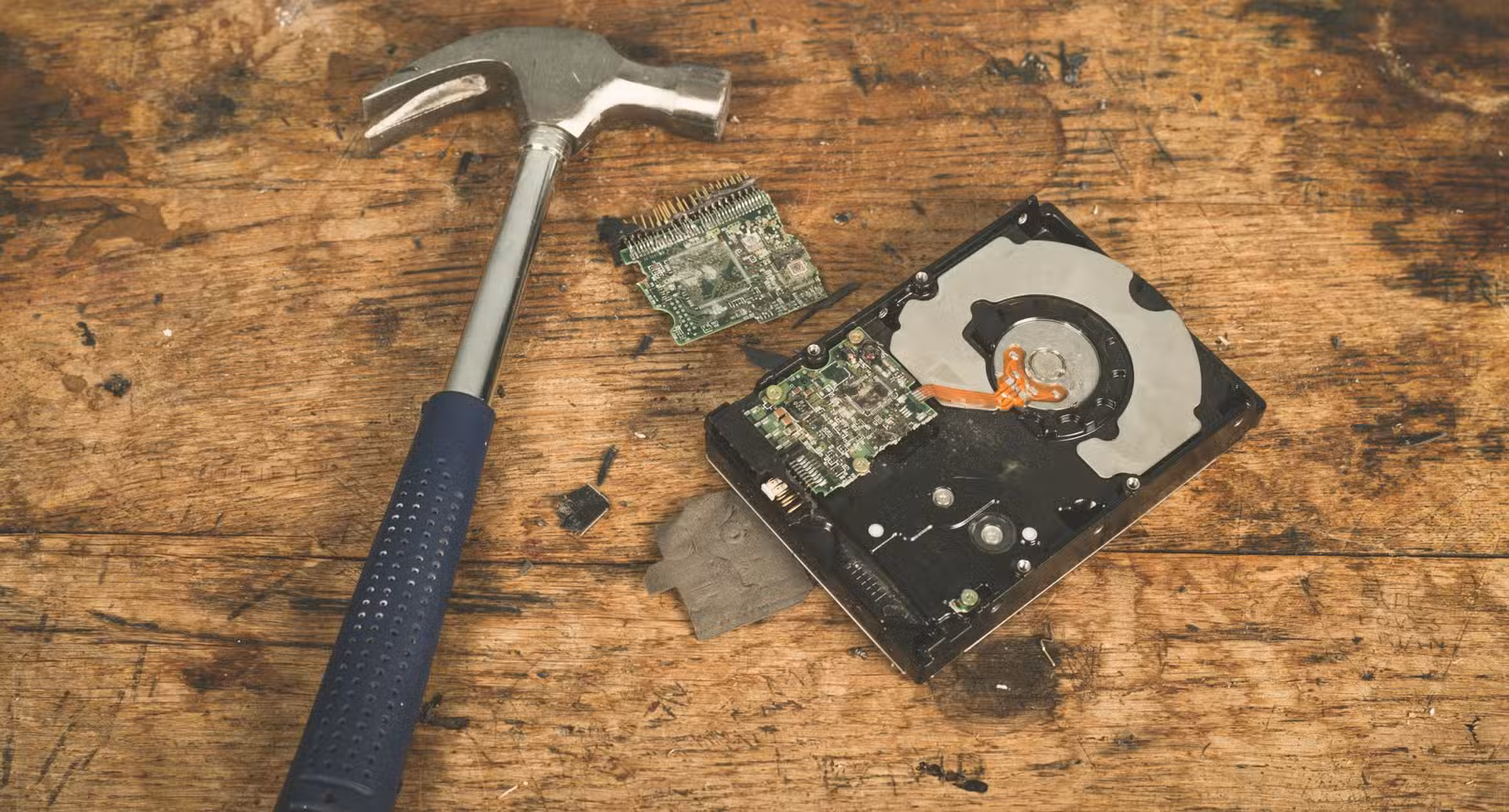 A hammer and a smashed computer harddrive on a wooden surface.