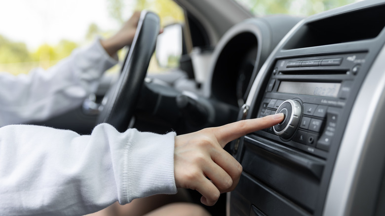 A person adjusts the stereo controls on a car's center console while seated behind the wheel.