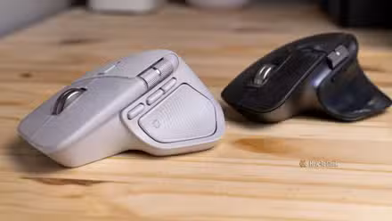 The white Logitech MX Master 4 next to a black MX Master 3S viewed from the left side.