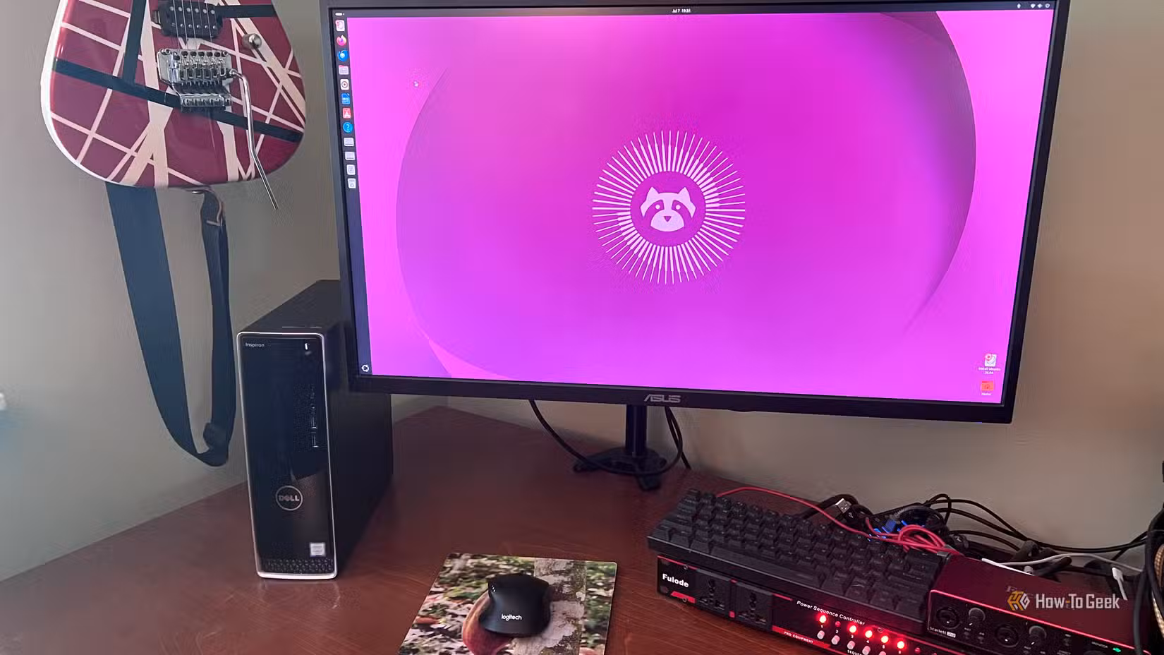 AN image of a computer running Ubuntu Linuxsitting on a desktop with a keyboard and a mouse. On the left there is a guitar hanging on the wall.