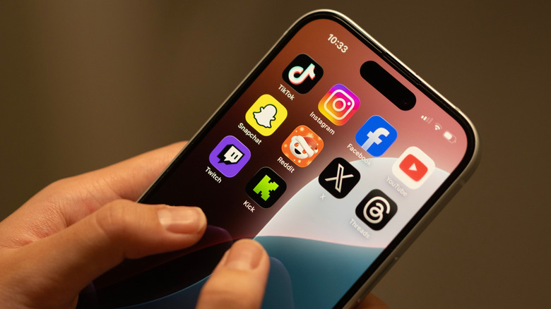 Hands holding an iPhone with various social media app icons on the home screen.