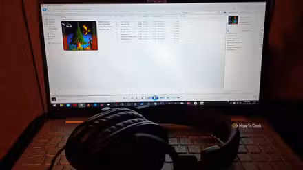 A pair of large, black headphones sitting on the keyboard of a laptop with a screen displaying Windows Media Player and a picture of a tree.
